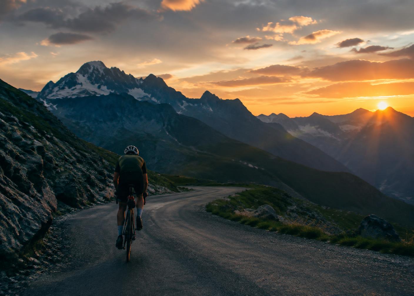 A cyclist climbing a mountain road at sunset