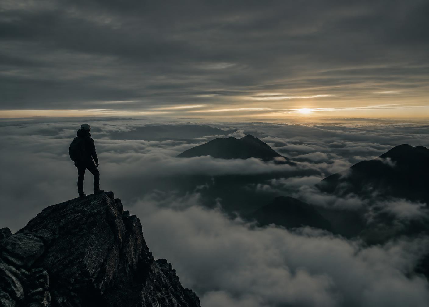 A climber on a summit rock above a sea of clouds